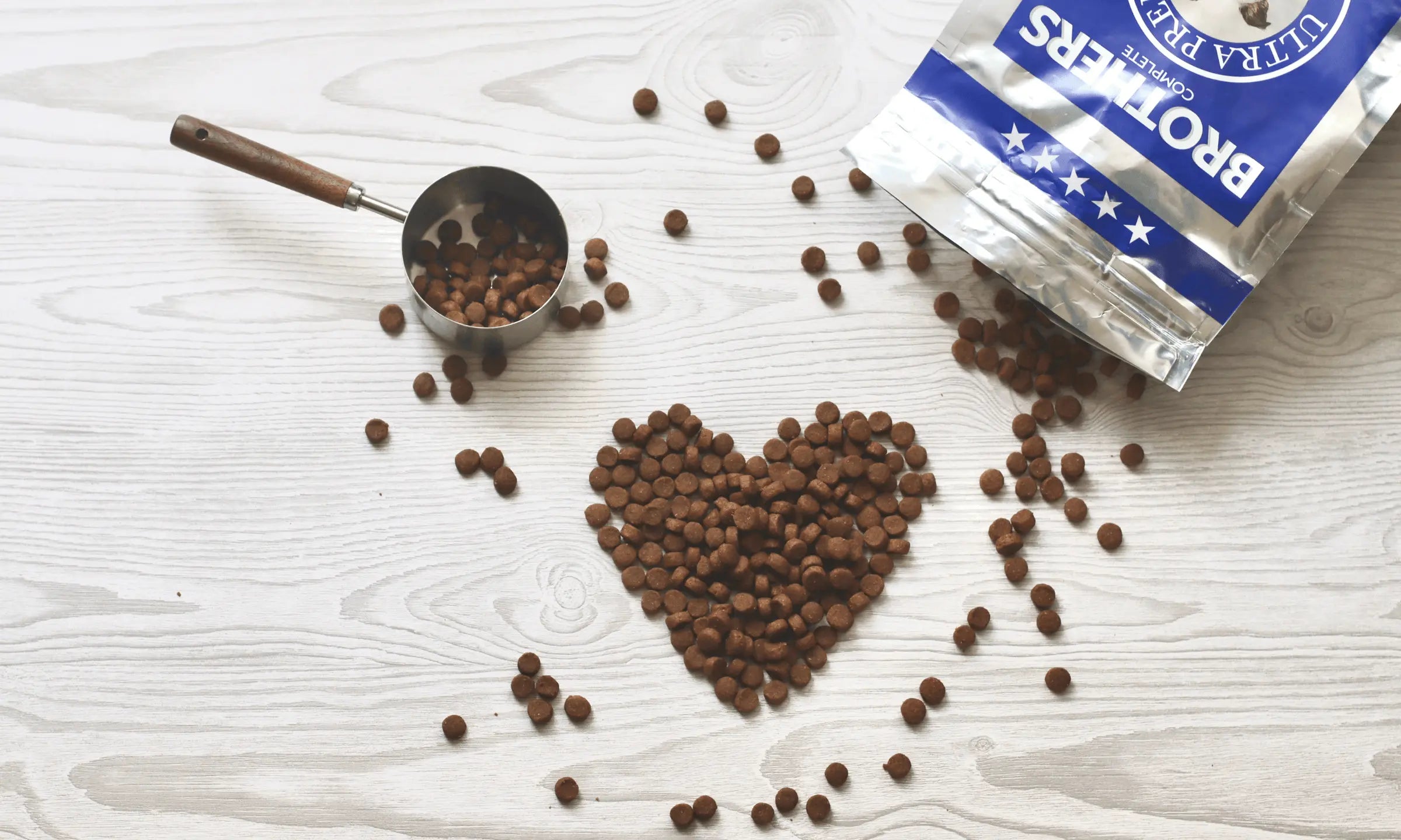 Brothers dog food kibble arranged in a heart shape beside a measuring cup and an open bag of Brothers dog food